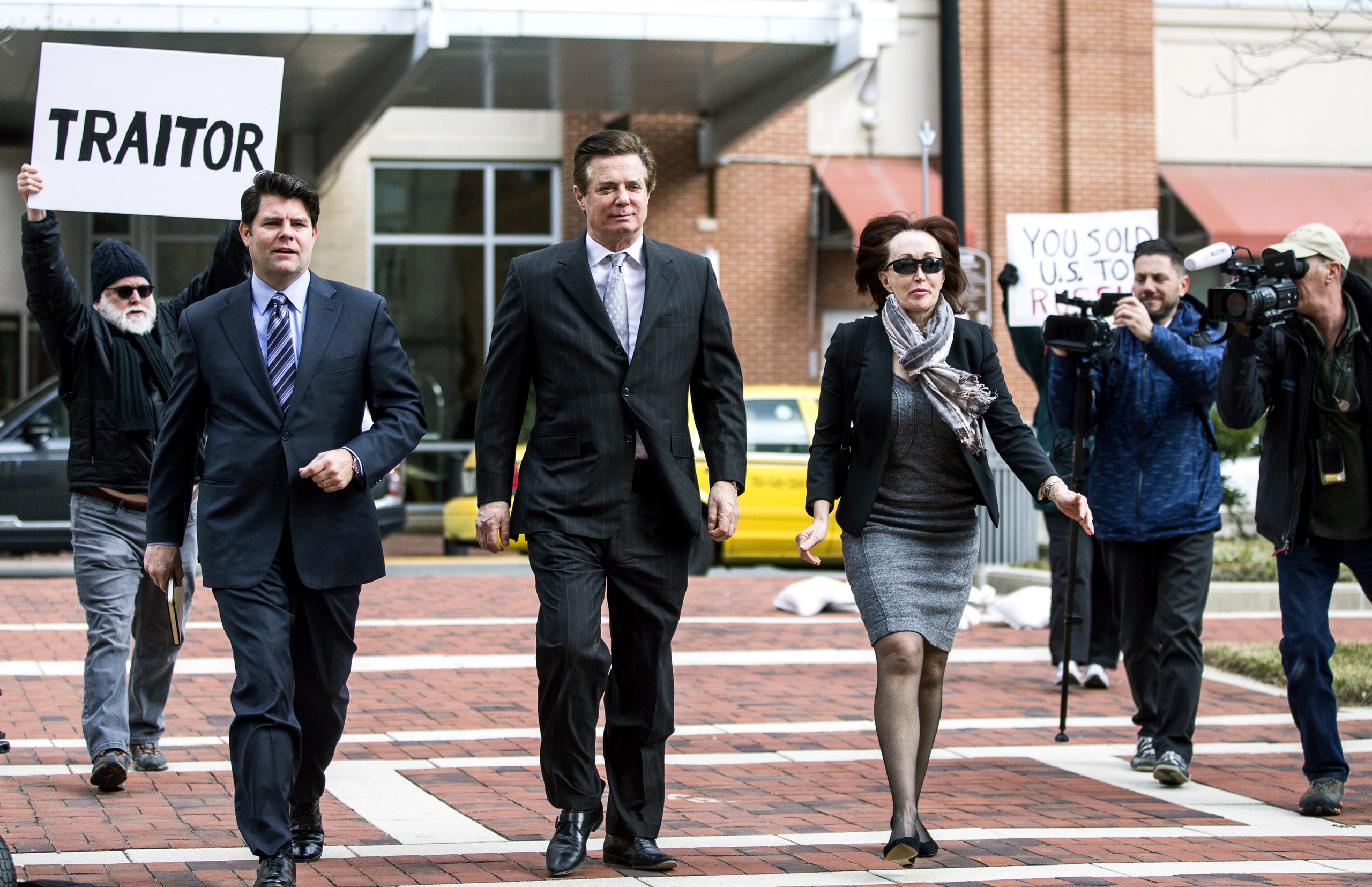 Paul Manafort walks beside a man holding a sign reading “Traitor.”